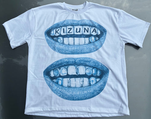 A white short-sleeve t-shirt laid flat on a dark gray surface, featuring a blue graphic of two open mouths with teeth, where the top mouth has the word 'KIZUNA' spelled out in letter tiles.