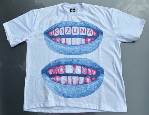 A white short-sleeve t-shirt laid flat on a dark gray surface, featuring a graphic of two blue lips with teeth. The top lip has the word 'KIZUNA' spelled out in letter tiles on the teeth, and the bottom lip has alternating pink and white teeth.